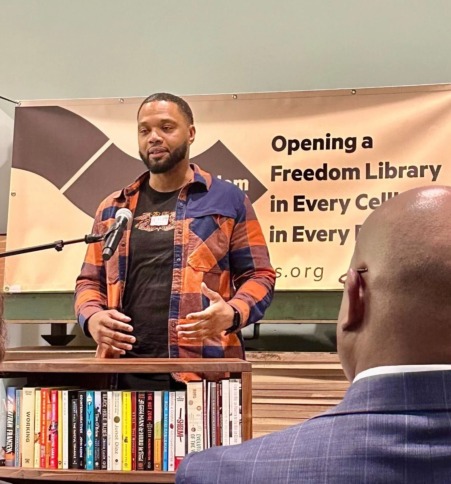 Freedom Reads Library Production Assistant Michael Byrd speaks at a microphone in front of a Freedom Library in the Freedom Reads office.