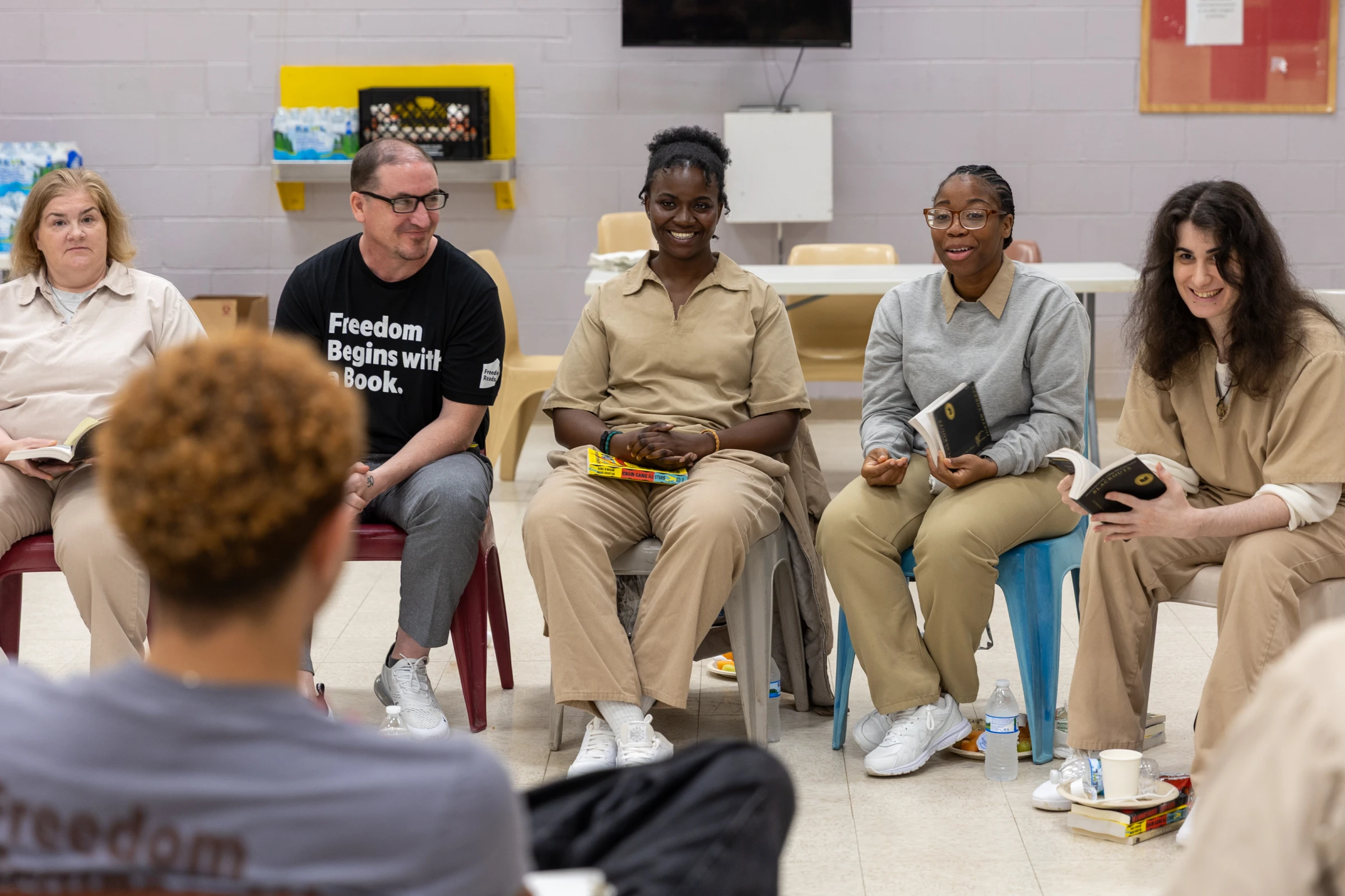 Women wearing khaki prison uniforms sit in a circle with Freedom Reads team discussing books